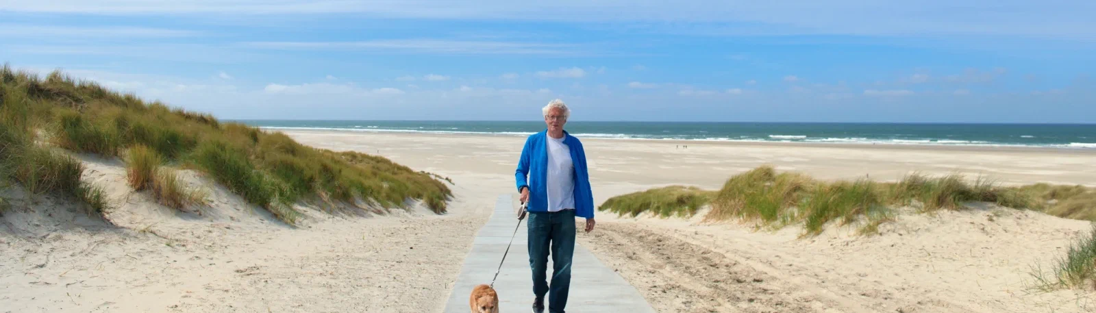 Oudere man laat hond uit op het strand