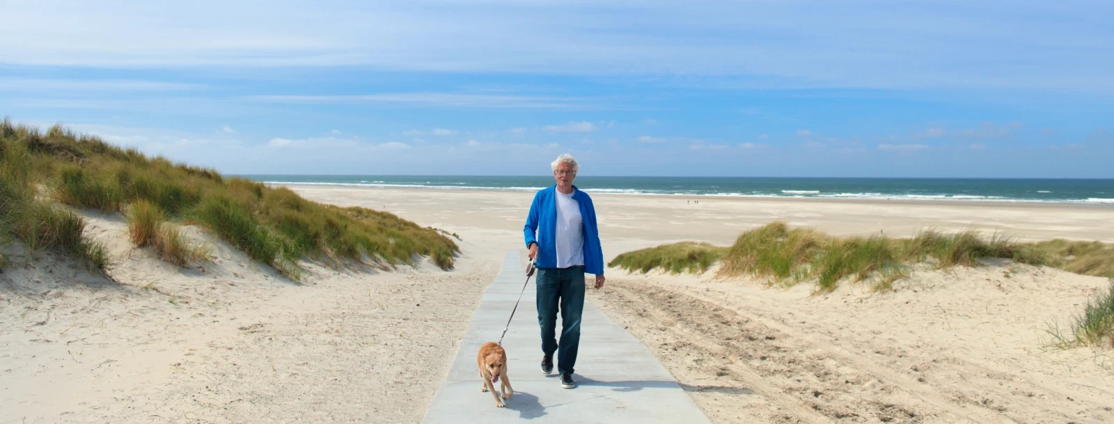 Oudere man laat hond uit op het strand