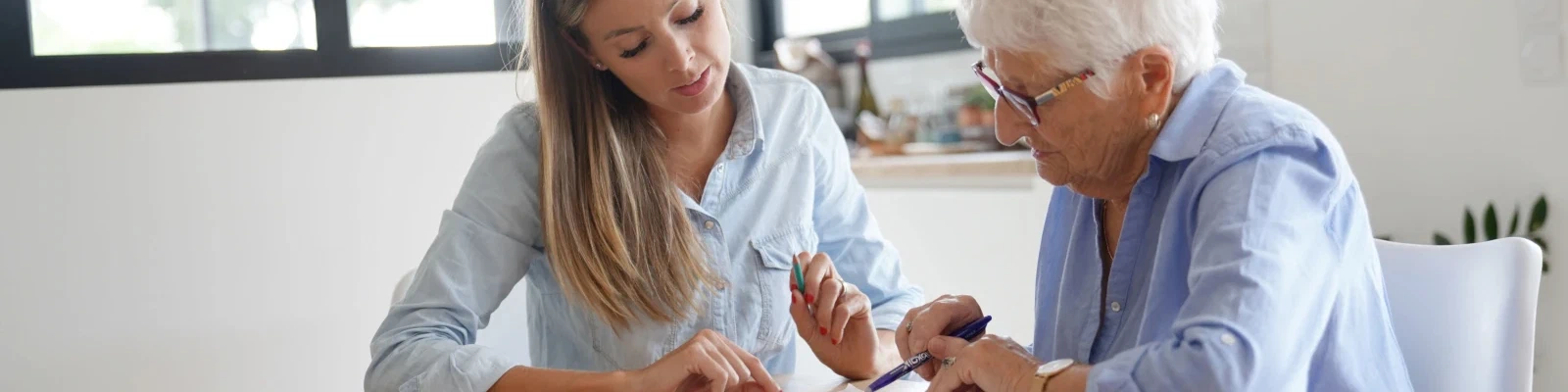 Vrouw helpt oudere moeder met het invullen van papierwerk aan tafel